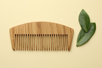 Photo of Wooden comb and leaves on beige background, flat lay