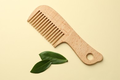 Photo of Wooden comb and leaves on beige background, flat lay