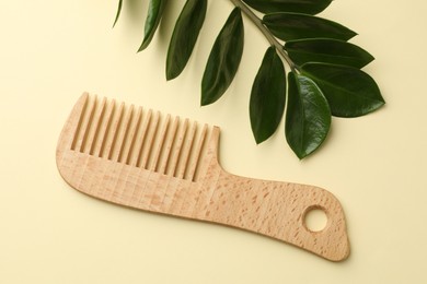 Photo of Wooden comb and branch with leaves on beige background, flat lay