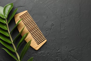 Photo of Wooden comb and branch with leaves on dark textured table, flat lay. Space for text