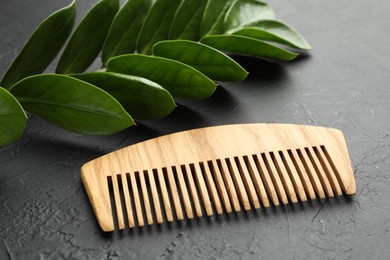 Photo of Wooden comb and branch with leaves on dark textured table, closeup