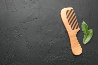 Photo of Wooden comb and leaves on dark textured table, flat lay. Space for text