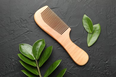 Photo of Wooden comb and branch with leaves on dark textured table, flat lay