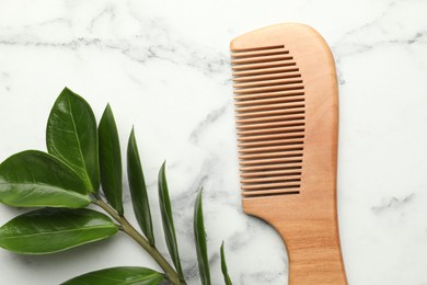 Photo of Wooden comb and branch with leaves on white marble table, flat lay