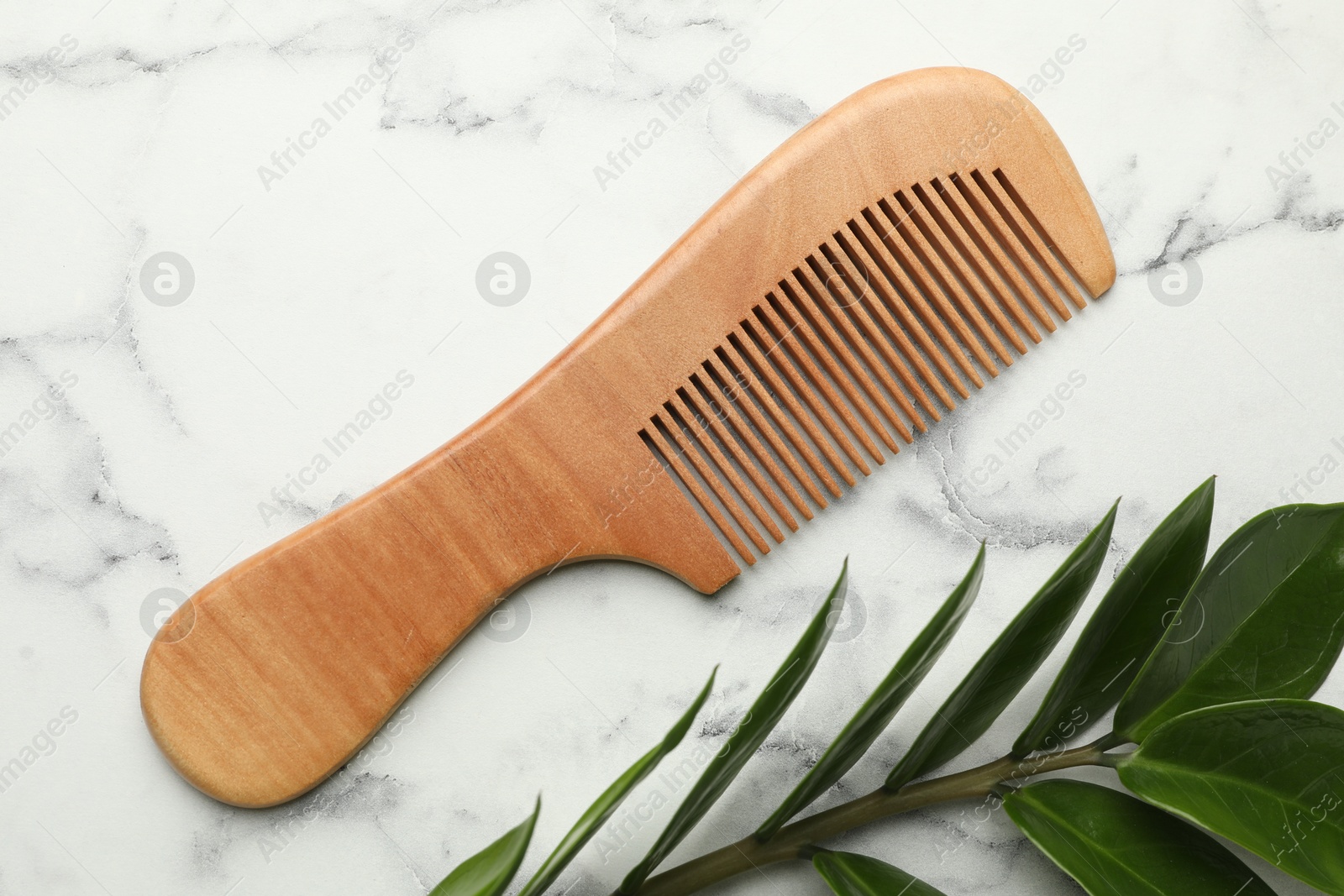 Photo of Wooden comb and branch with leaves on white marble table, flat lay