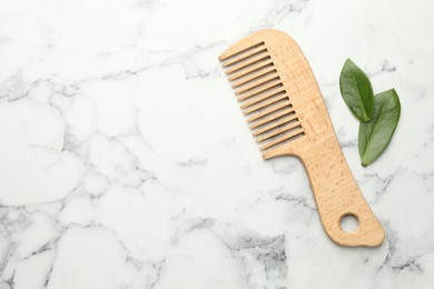 Photo of Wooden comb and leaves on white marble table, flat lay. Space for text