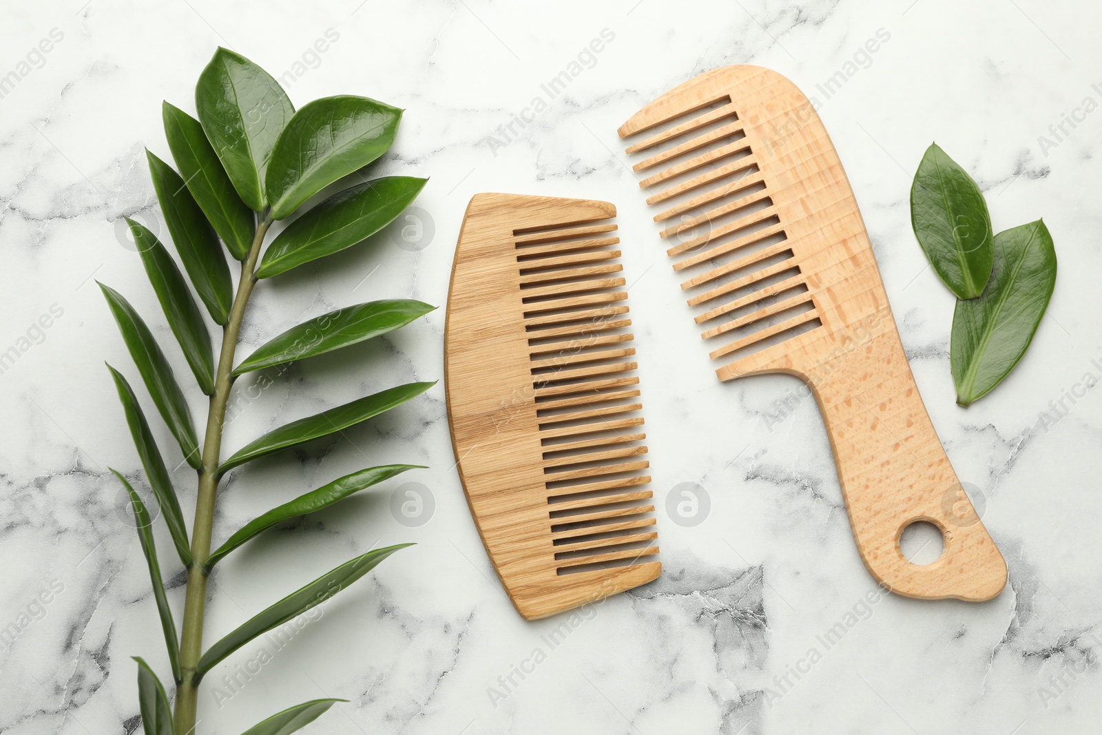 Photo of Wooden combs and branch with leaves on white marble table, flat lay