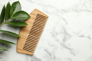 Photo of Wooden comb and branch with leaves on white marble table, flat lay. Space for text