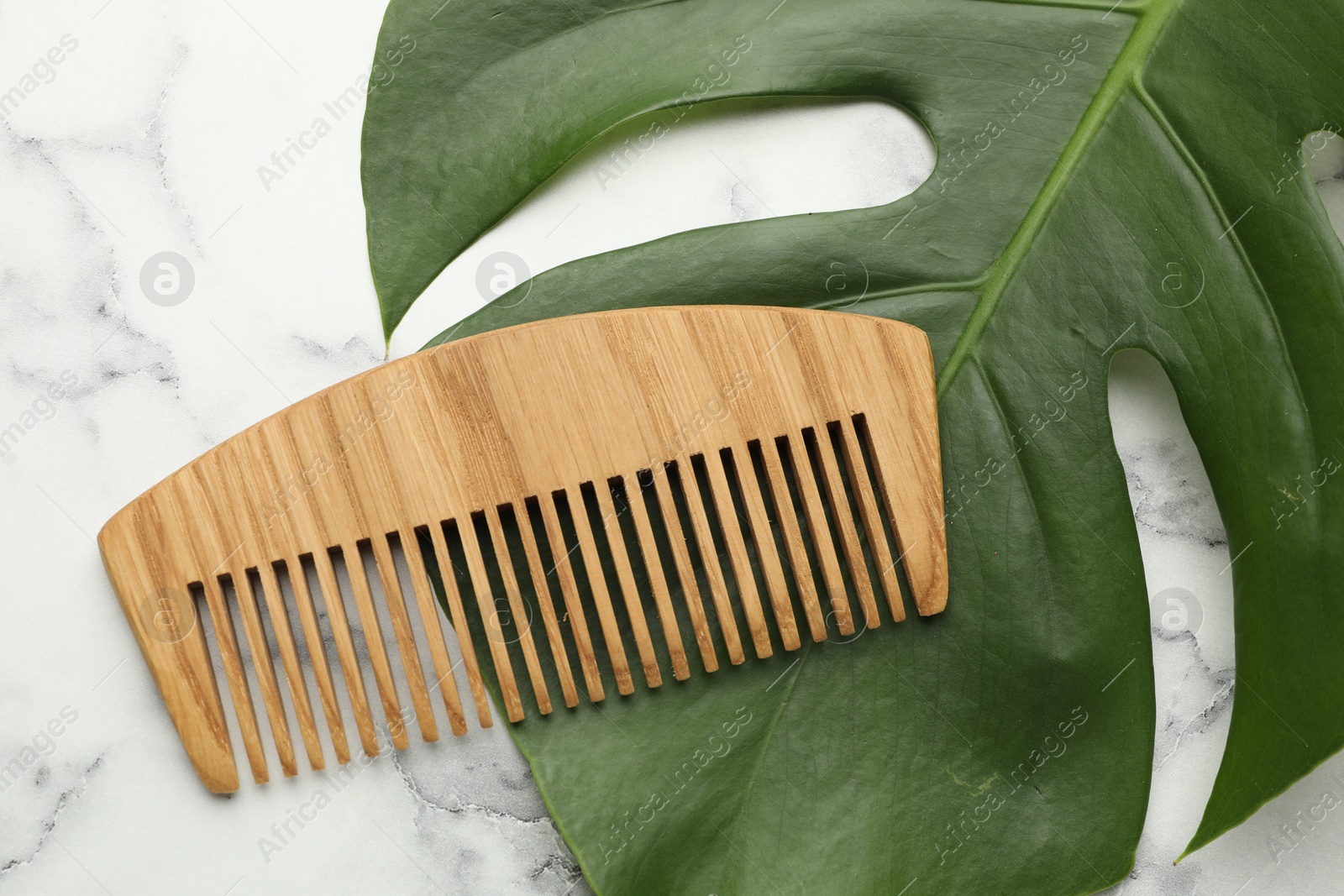 Photo of Wooden comb and monstera leaf on white marble table, flat lay