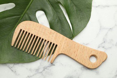 Photo of Wooden comb and monstera leaf on white marble table, flat lay