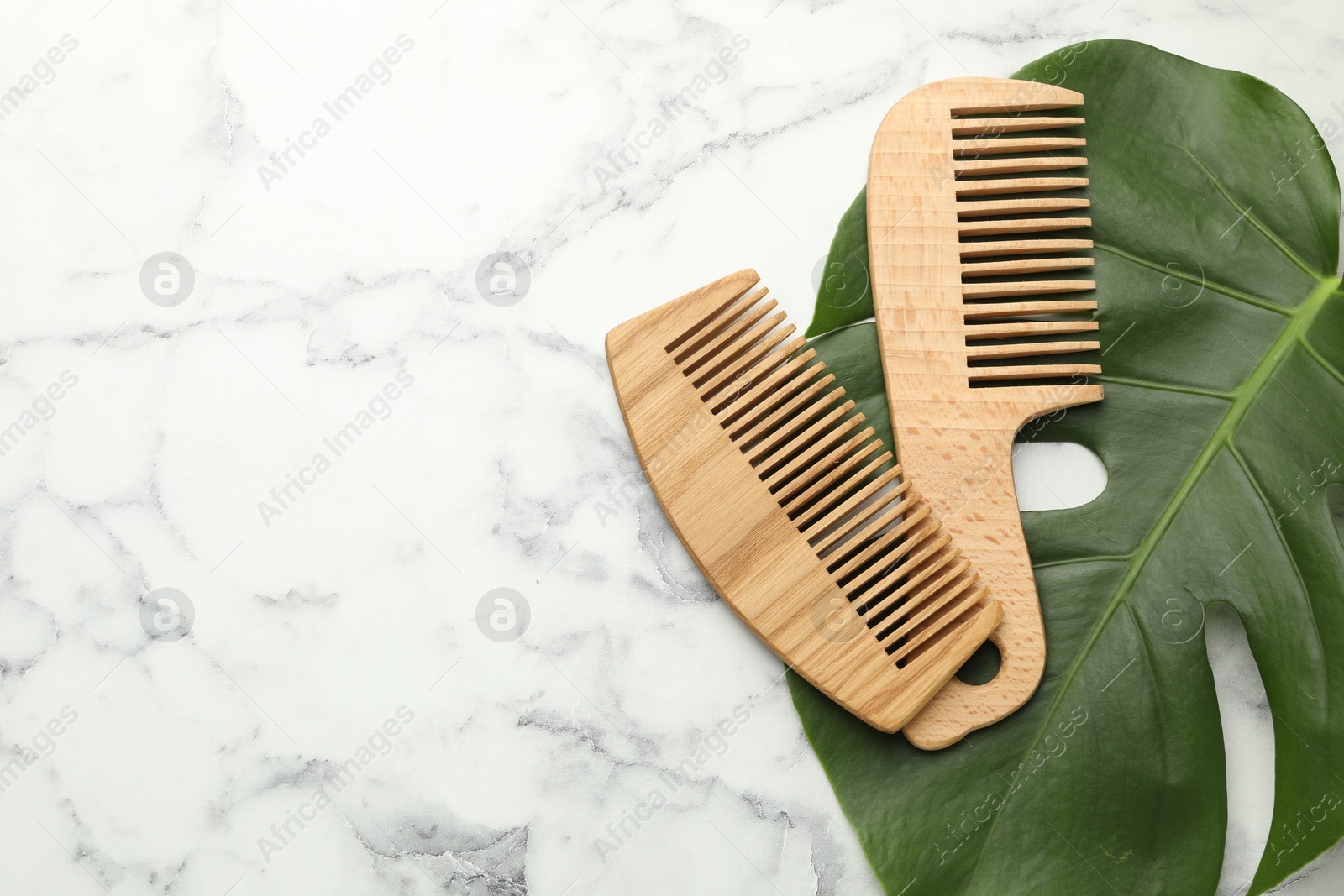 Photo of Wooden combs and monstera leaf on white marble table, flat lay. Space for text