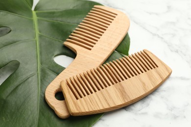 Photo of Wooden combs and monstera leaf on white marble table, closeup