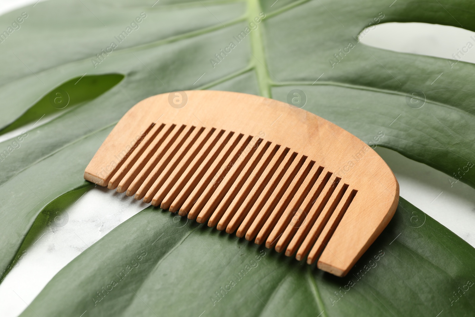 Photo of Wooden comb and monstera leaf on white table, closeup