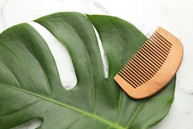 Photo of Wooden comb and monstera leaf on white marble table, top view