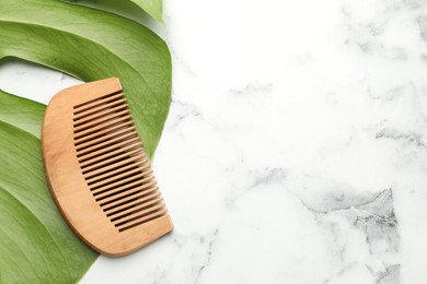 Photo of Wooden comb and monstera leaf on white marble table, top view. Space for text