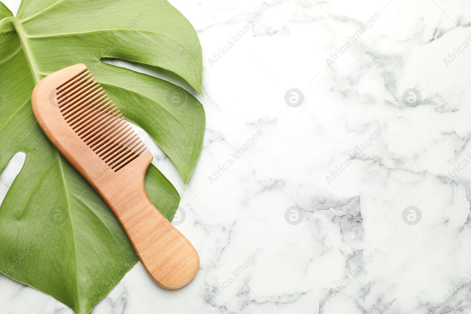 Photo of Wooden comb and monstera leaf on white marble table, top view. Space for text