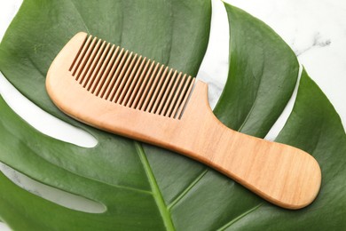 Photo of Wooden comb and monstera leaf on white marble table, top view