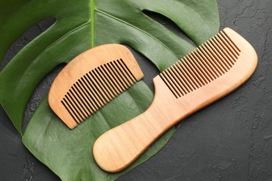 Photo of Wooden combs and monstera leaf on dark textured table, flat lay