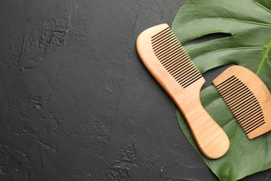 Photo of Wooden combs and monstera leaf on dark textured table, top view. Space for text