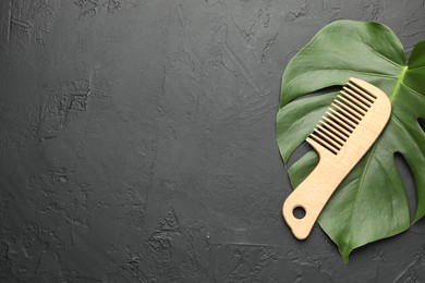 Photo of Wooden comb and monstera leaf on dark textured table, top view. Space for text