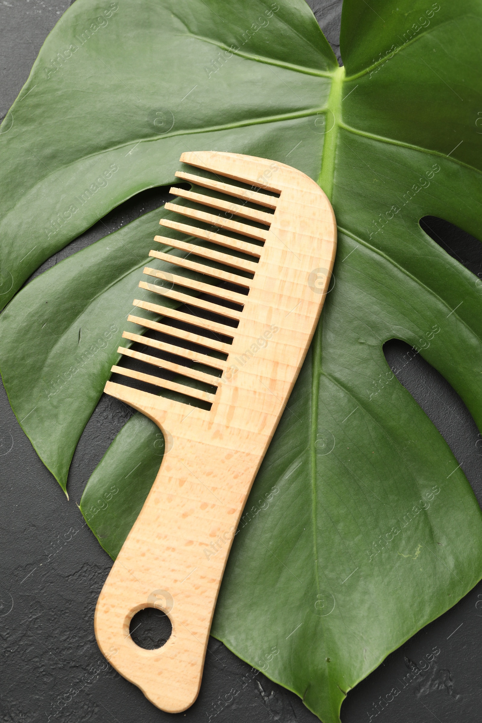 Photo of Wooden comb and monstera leaf on dark textured table, top view