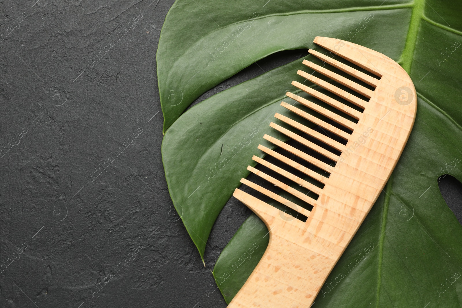 Photo of Wooden comb and monstera leaf on dark textured table, top view. Space for text