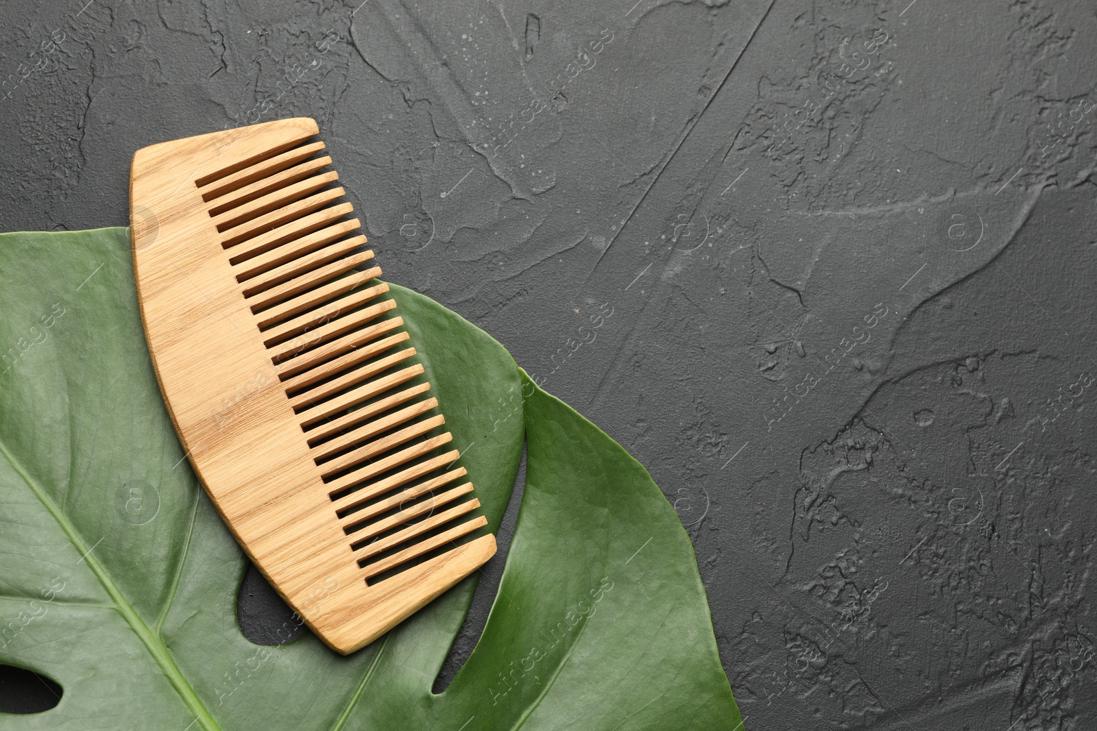 Photo of Wooden comb and monstera leaf on dark textured table, top view. Space for text