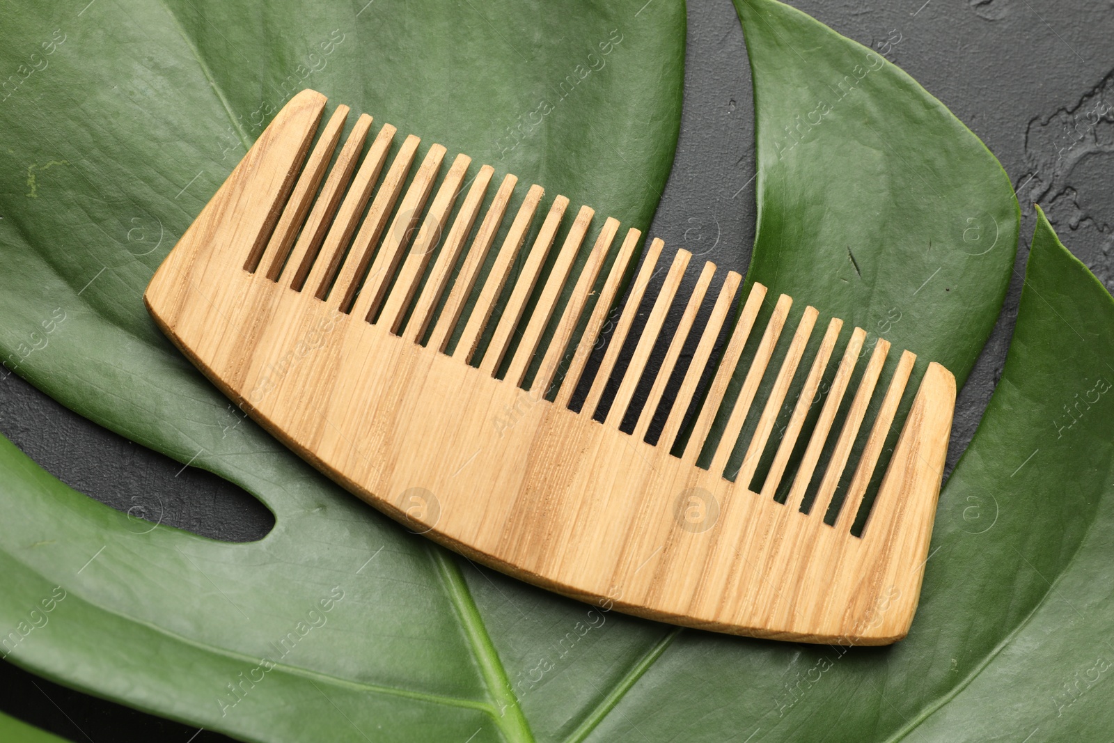 Photo of Wooden comb and monstera leaf on dark textured table, top view