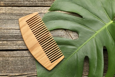 Photo of Comb and monstera leaf on wooden table, top view