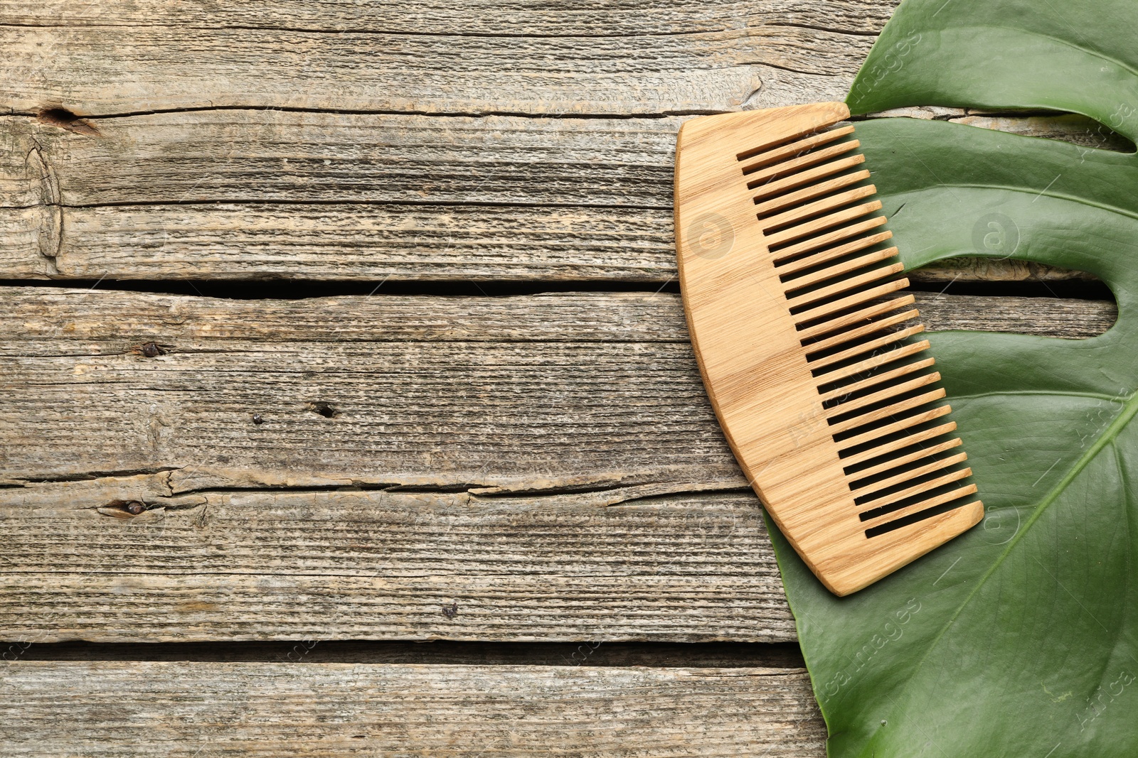 Photo of Comb and monstera leaf on wooden table, top view. Space for text