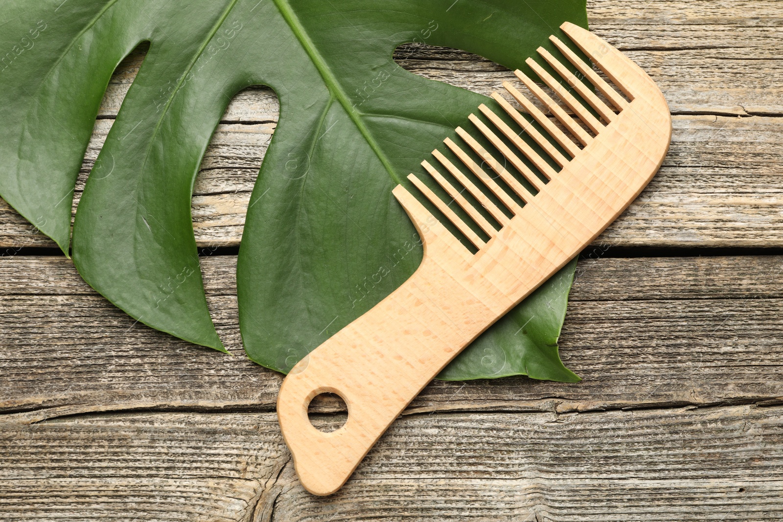 Photo of Comb and monstera leaf on wooden table, top view