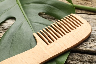 Photo of Comb and monstera leaf on wooden table, closeup