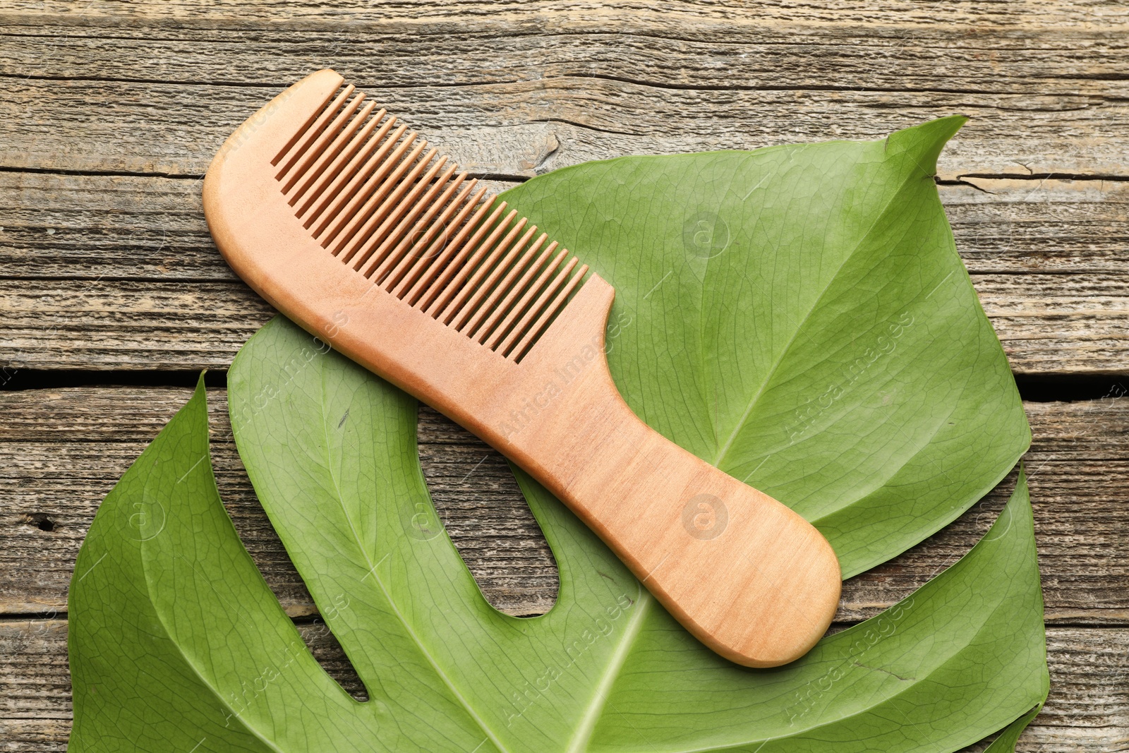 Photo of Comb and monstera leaf on wooden table, top view