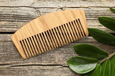 Photo of Comb and branch with leaves on wooden table, flat lay