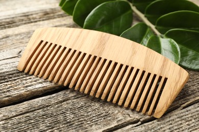 Photo of Comb and branch with leaves on wooden table, closeup