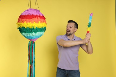 Photo of Emotional man hitting colorful pinata with stick on yellow background