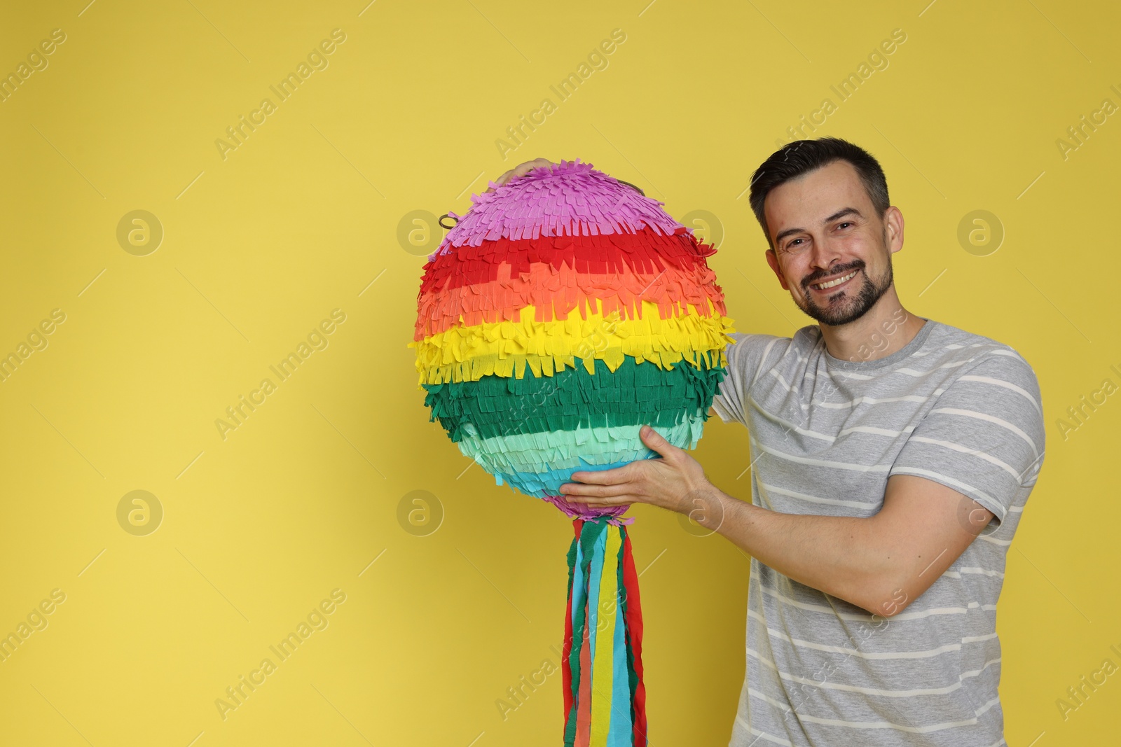 Photo of Happy man with colorful pinata on yellow background, space for text