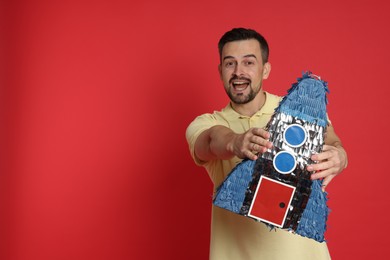 Photo of Happy man with rocket shaped pinata on red background, space for text