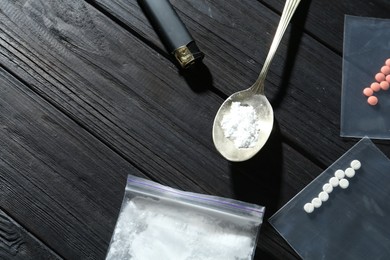 Photo of Drug addiction. Plastic bag with powder, spoon cigarette lighter and pills on black wooden table, flat lay. Space for text