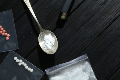 Photo of Drug addiction. Plastic bag with powder, spoon cigarette lighter and pills on black wooden table, flat lay. Space for text