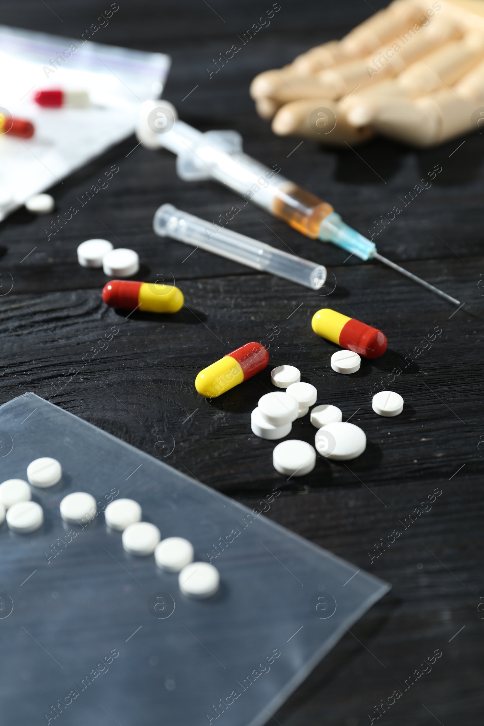 Photo of Drug addiction. Plastic bag with pills and syringe on black wooden table, closeup