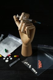 Photo of Drug addiction. Mannequin hand with syringe and pills on black wooden table against dark background