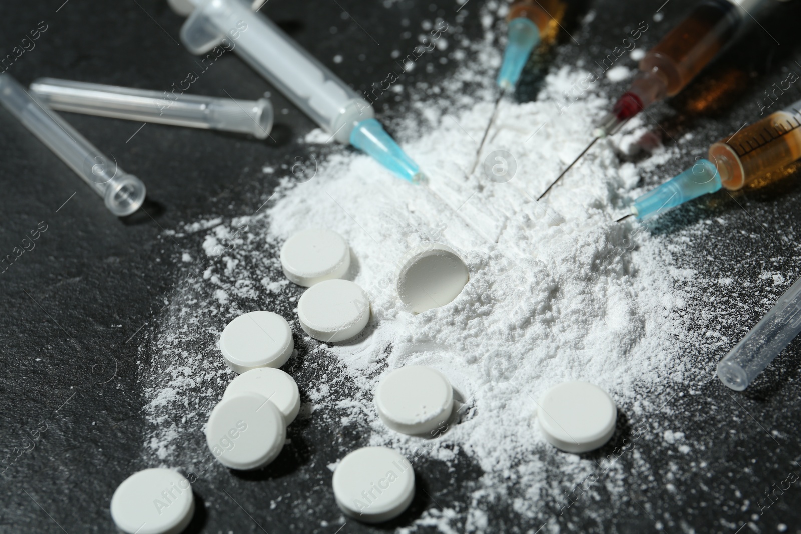 Photo of Drug addiction. Powder, pills and syringes on gray textured table, closeup