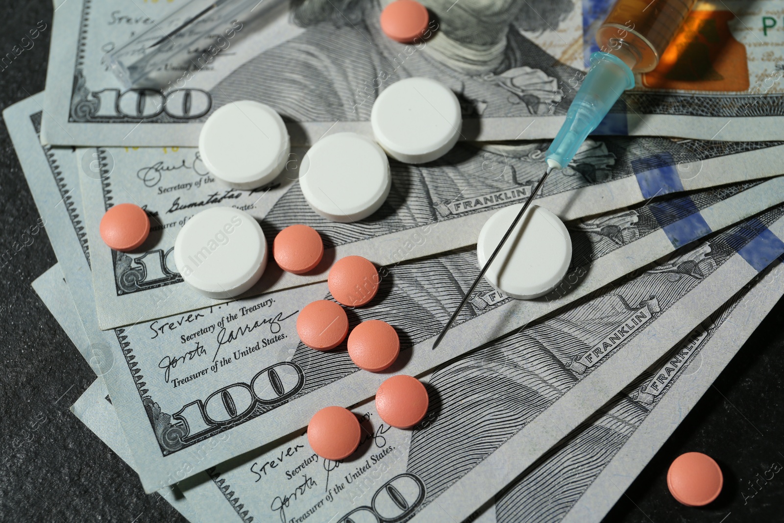 Photo of Drug addiction. Dollar banknotes, pills and syringe on gray table, above view