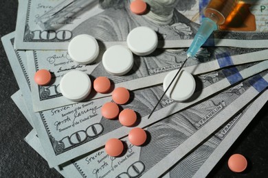 Photo of Drug addiction. Dollar banknotes, pills and syringe on gray table, above view