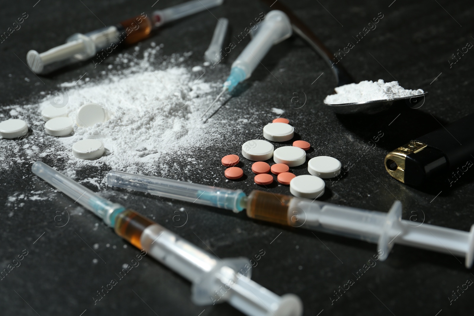 Photo of Drug addiction. Spoon with powder, pills, syringes and cigarette lighter on gray table, closeup