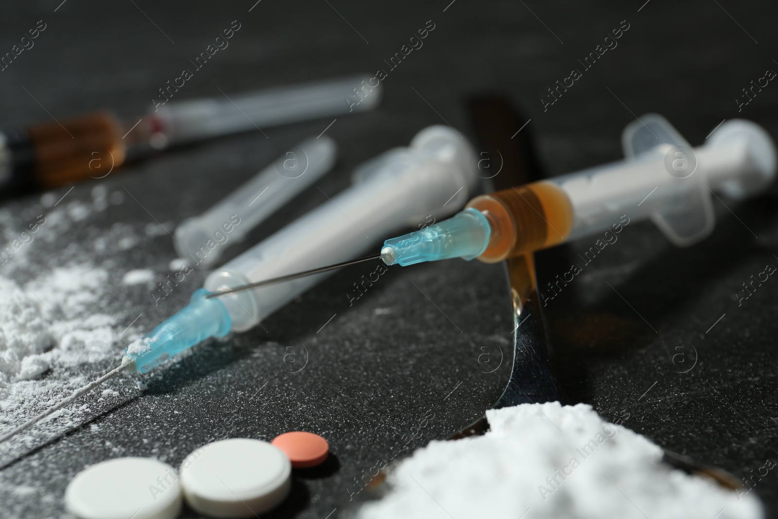 Photo of Drug addiction. Spoon with powder, pills and syringes on gray table, closeup