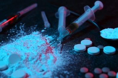 Photo of Drug addiction. Powder, pills and syringes on dark table in neon lights, closeup