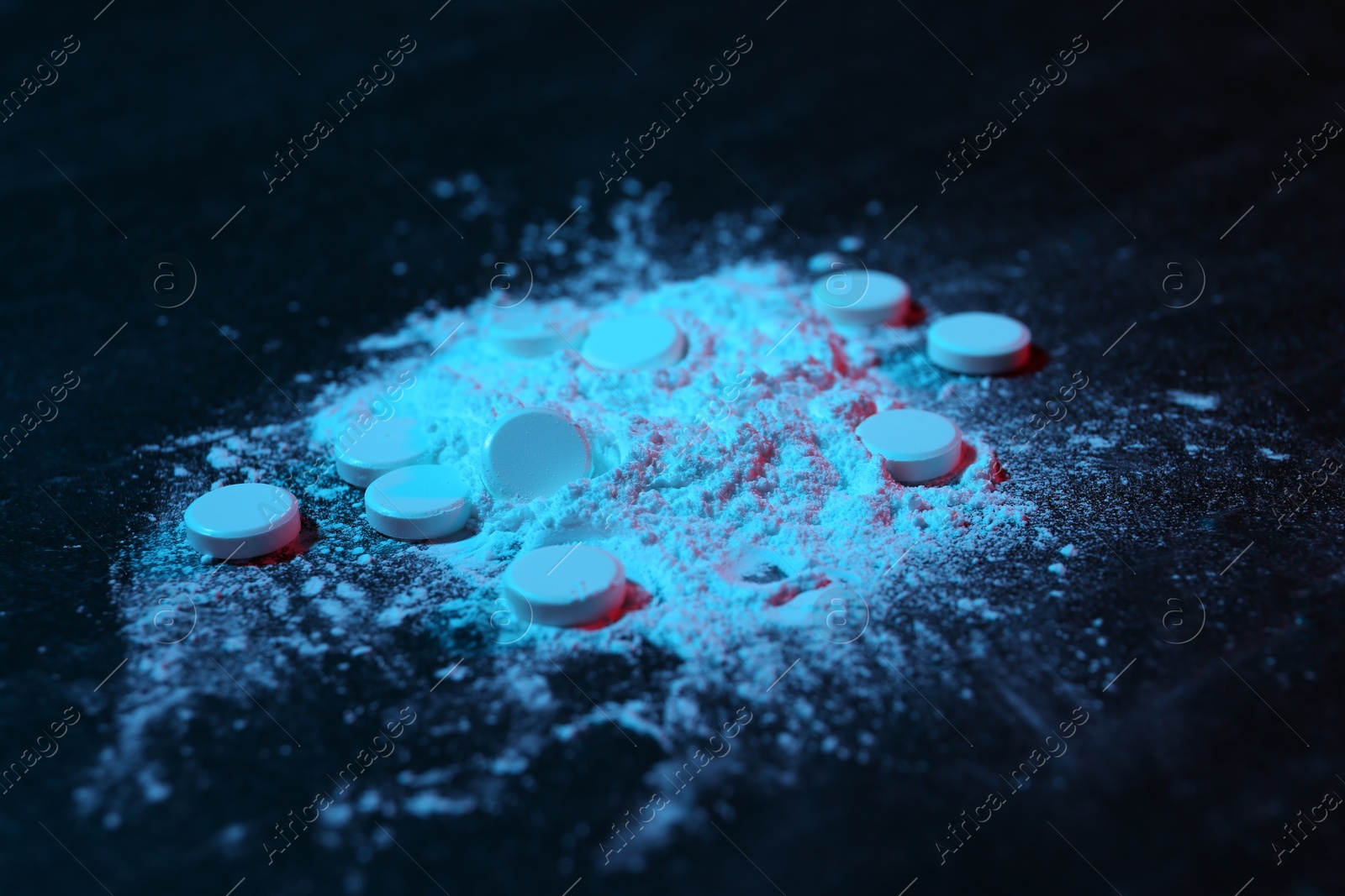 Photo of Drug addiction. Powder and pills on dark table in neon lights, closeup