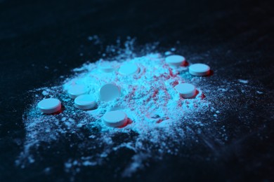 Photo of Drug addiction. Powder and pills on dark table in neon lights, closeup